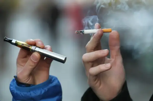 Deux mains tiennent une cigarette électronique et une cigarette allumée, symbolisant les différentes formes de consommation de nicotine et leur origine.
