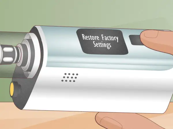 Main d'une personne tenant un appareil électronique avec un écran affichant "Restore Factory Settings". L'atomizer est visible sur le côté gauche.
