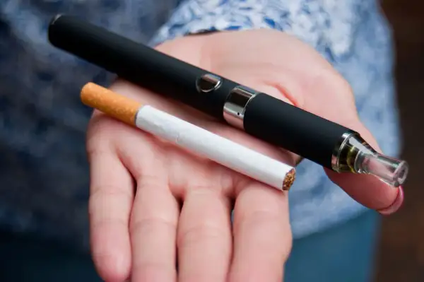 Témoignage arrêt tabac : une cigarette électronique et une cigarette classique sont tenues dans une main, symbolisant le passage à une alternative.