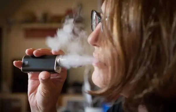 Une femme tire sur sa cigarette électronique, mais elle ne tire plus. La vapeur s'échappe.